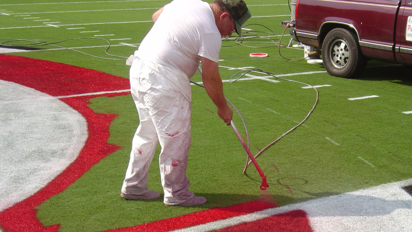 Person Painting A Logo On A Football Field 

